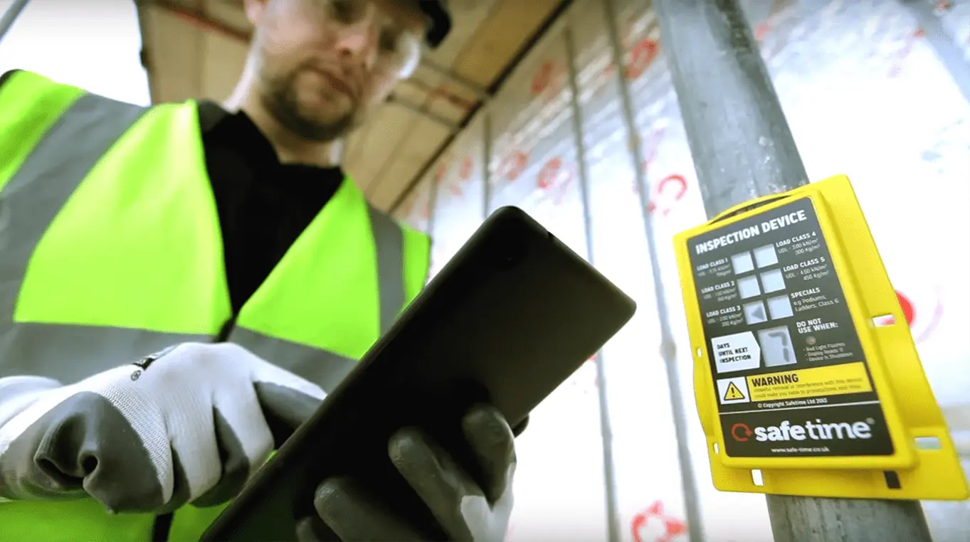 Construction worker scrolling on tablet next to an Inspect7® Device on a scaffolding tube.