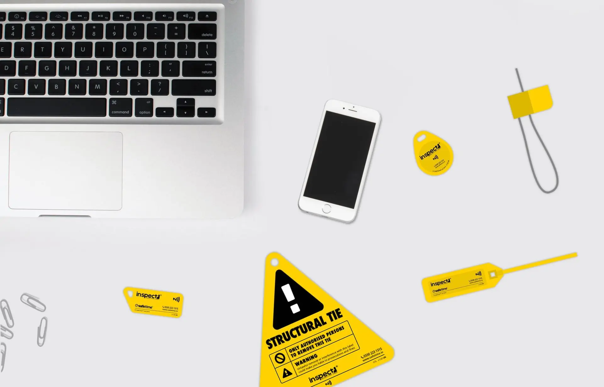 Inspect7® NFC inspection tags displayed on a desk a laptop and smartphone, showing the various tag shapes including a structural tie label, steel asset tags, zip tie tag and key fob tags. 